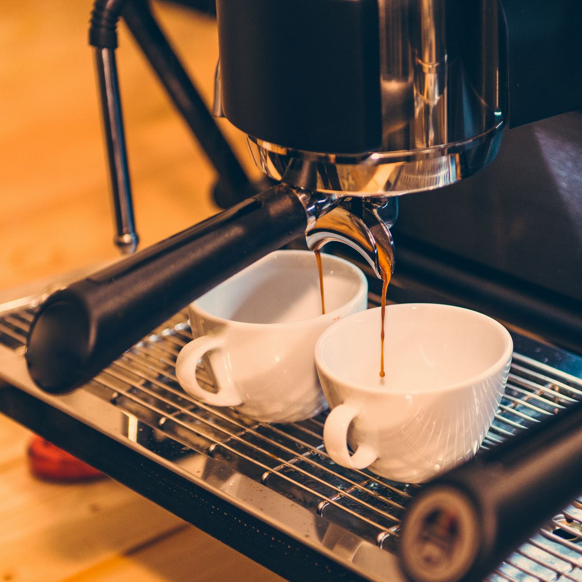 Espresso pouring into two cups on a stainless drip tray